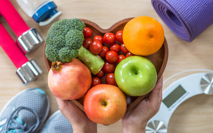 a person holding a heart shaped bowl of fruits and vegetables