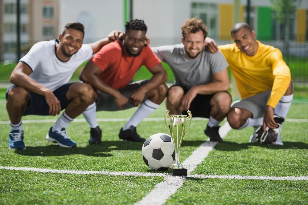 four men posing with a soccer ball on a field