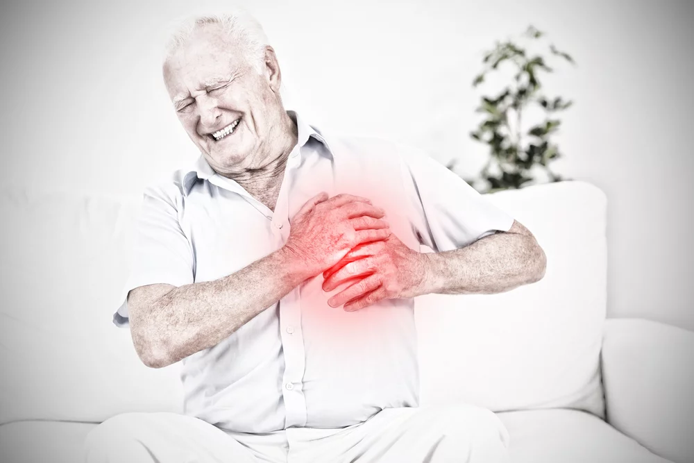 an older man sitting on a couch holding his heart