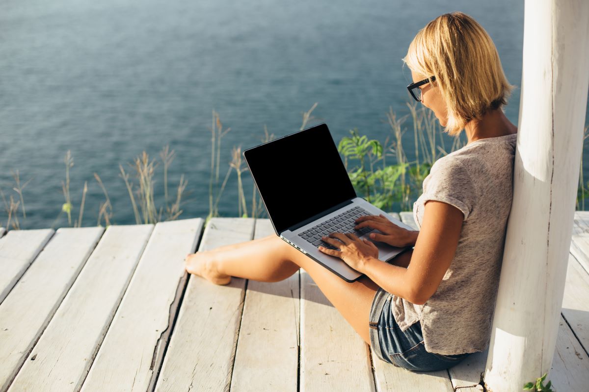 a woman sitting on a wooden deck with a laptop