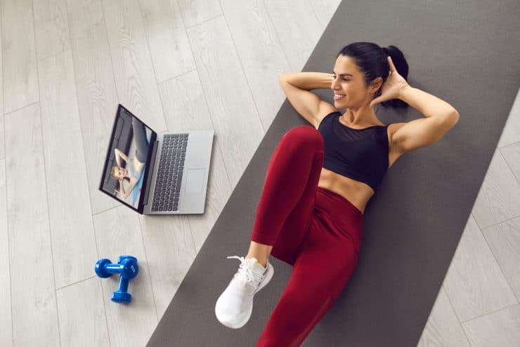 a woman is doing a workout on a mat with a laptop
