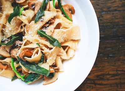 A plate of pappardelle pasta with mushrooms, greens, and grated cheese on a wooden table.
