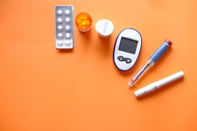 Diabetes management tools: glucose meter, insulin pen, syringes, and medication on an orange background.